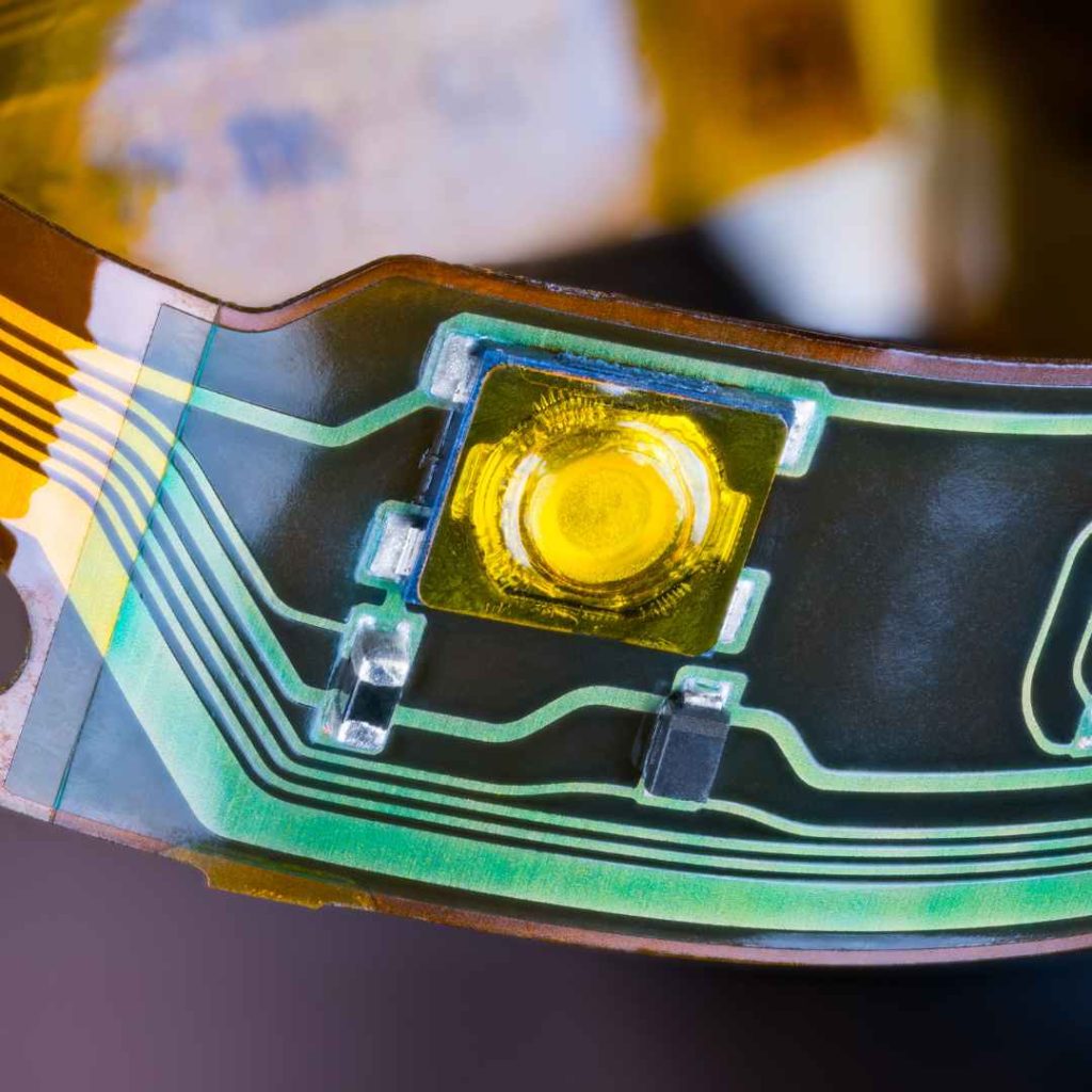 Detail of a flexible printed circuit, featuring thin traces and a surface-mounted LED, representing the growing trend of flexible electronics discussed in BENCOR's blog.