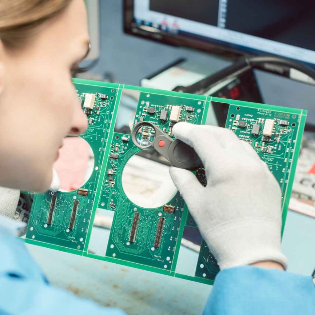 Technician inspecting a PCB using magnification and gloves.