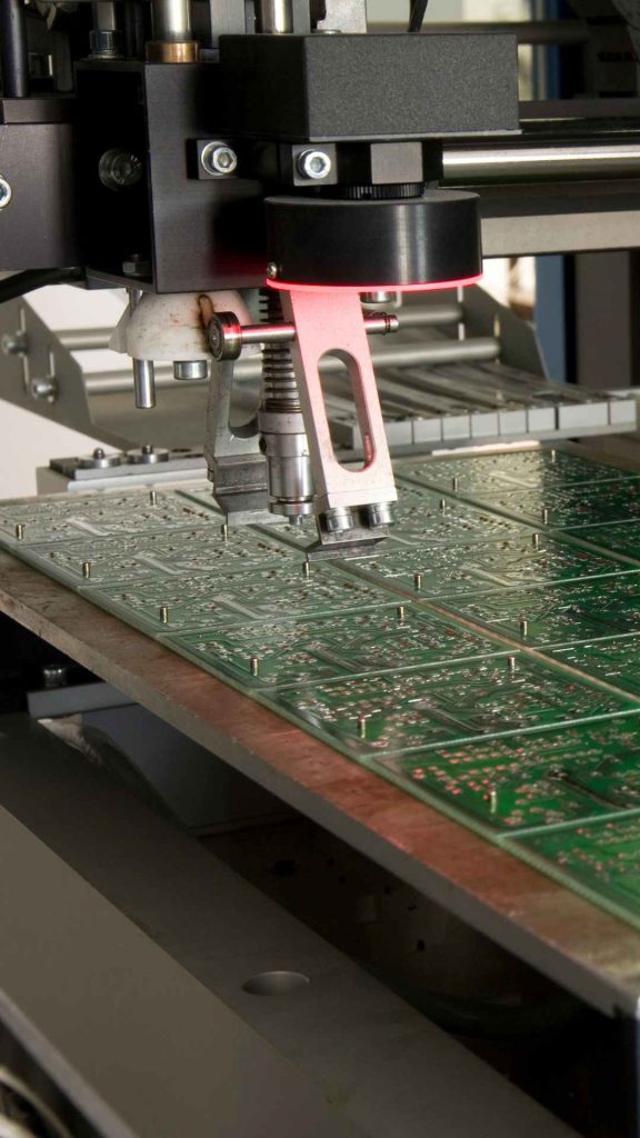 Advancements in Circuit Board Printing: What's New in PCB Manufacturing Technology? 1 Close-up of an automated PCB manufacturing machine with a robotic head and light guide precisely working on a panel of circuit boards, illustrating advancements in circuit board printing and fabrication technology.